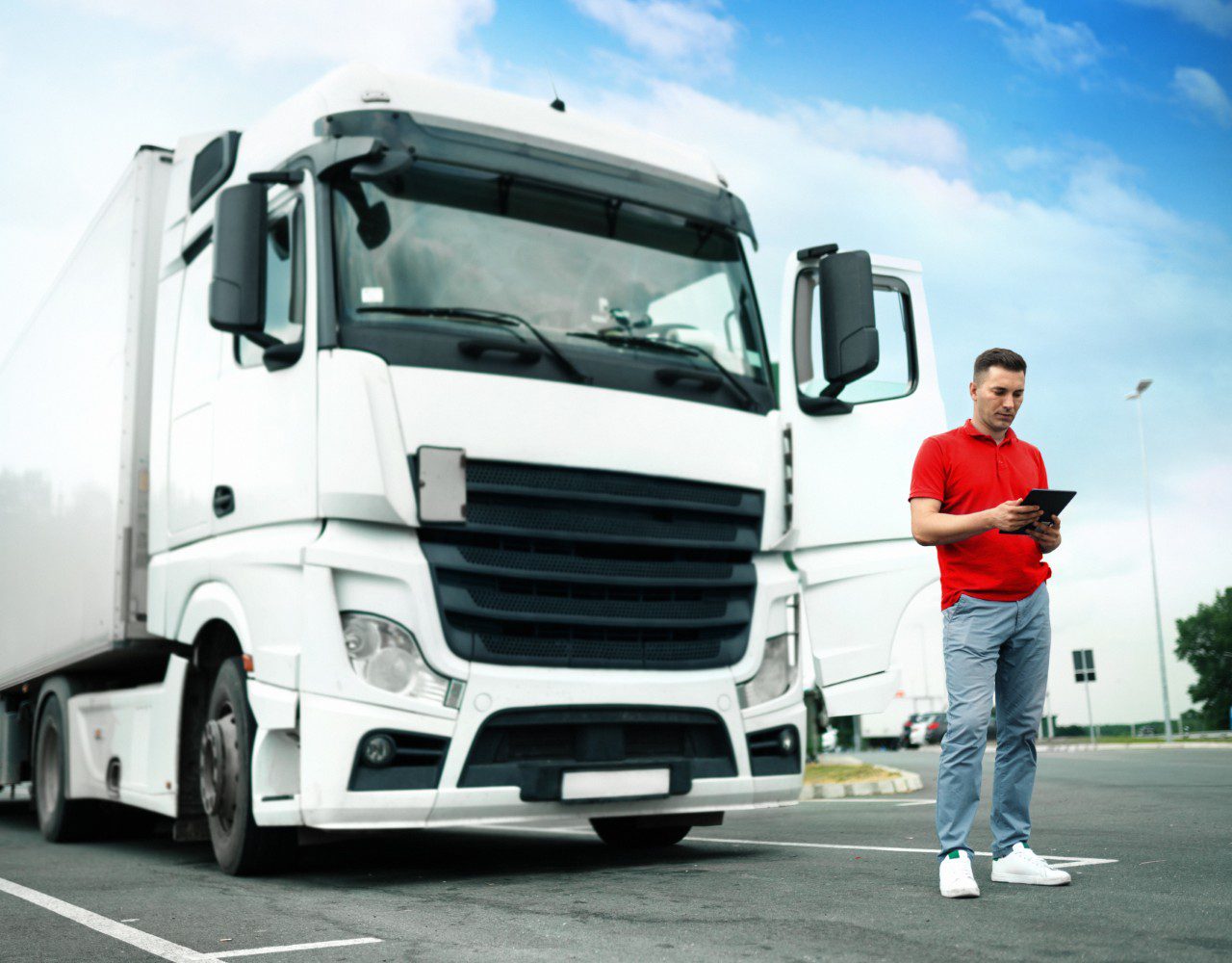 Truck driver checking tablet beside parked semi